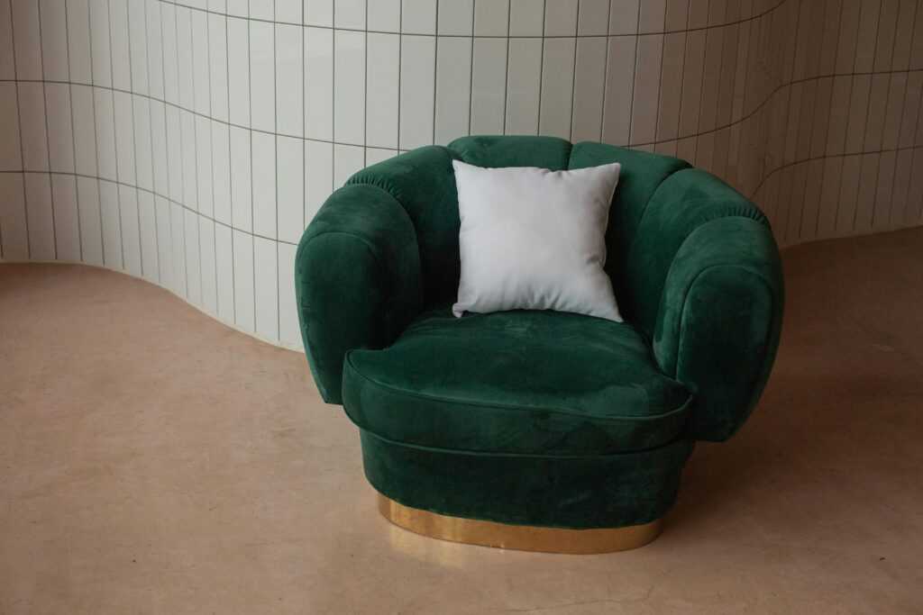 Luxurious green velvet armchair with a white pillow set against a stylish tiled backdrop for modern interiors.